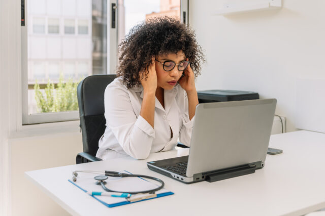 Stressed doctor suffering headache while working on laptop in clinic